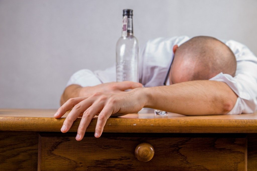 A man resting his head on a table while holding a bottle of liquor.