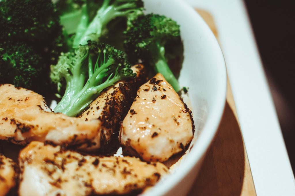 A closeup of chicken and broccoli in a white bowl.