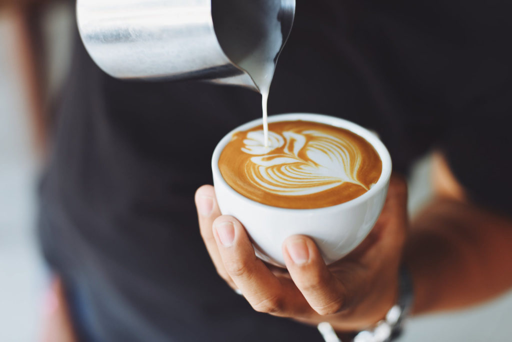 Someone pours foamy milk in a heart pattern into a mug full of coffee