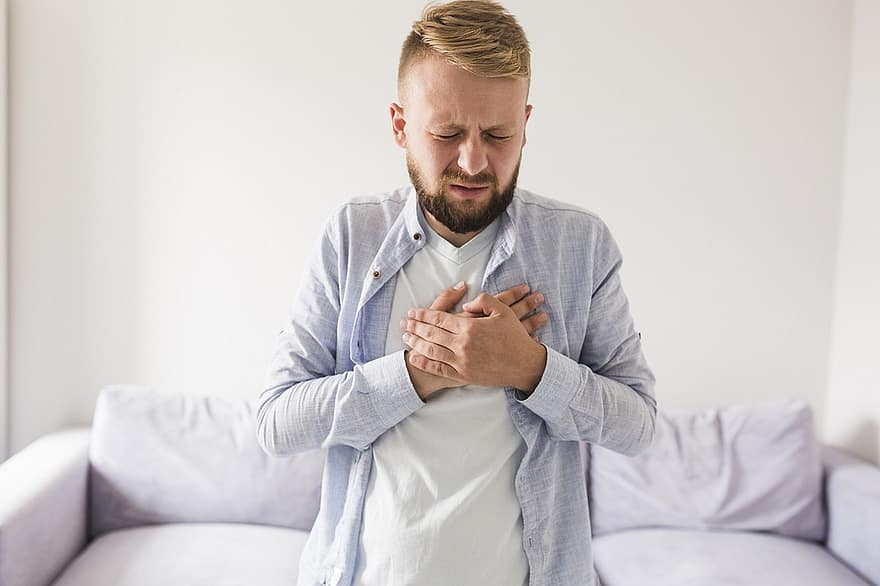 A man with blond hair in a white shirt putting his hands over his chest, demonstrating that he is experiencing heartburn, a common symptom of GERD.