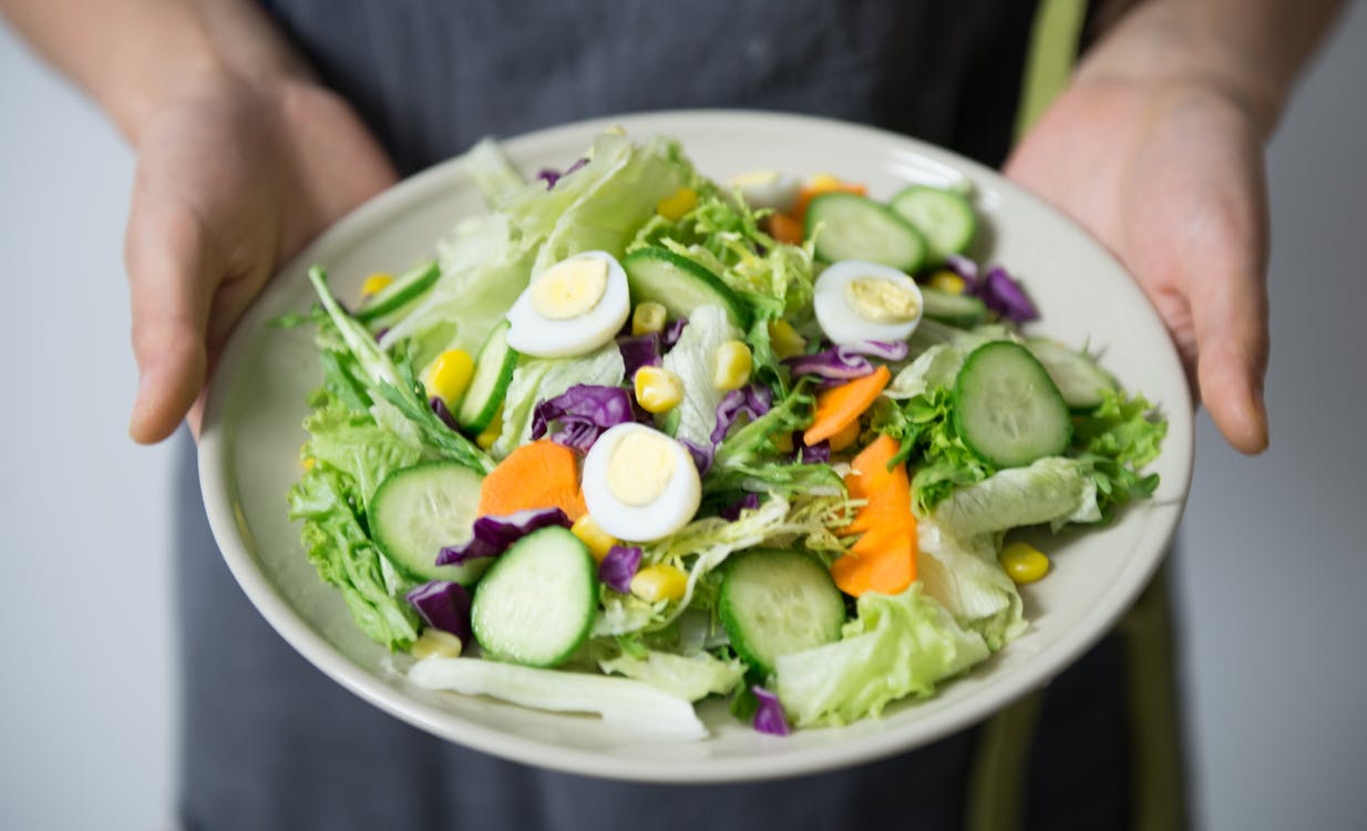 A person holding a bowl full of vegetable salad.