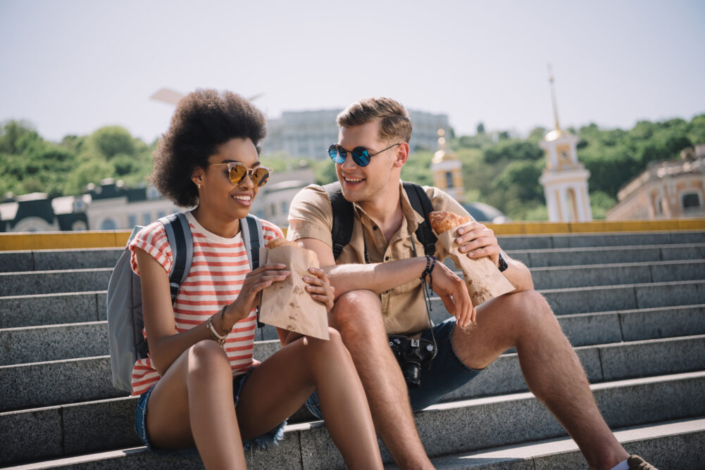 A pair of tourists having a snack while sitting on some steps.